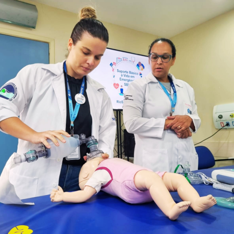 A imagem apresenta uma residente a frente com um suporte ventilatório no manequim de uma criança. 